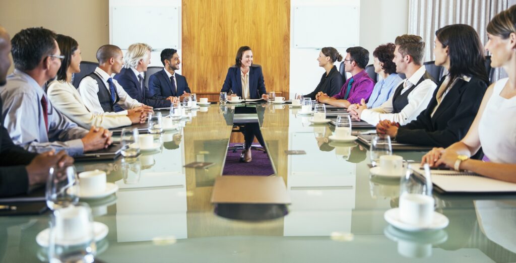 Conference participants looking at young woman sitting at head of conference table stock photo
