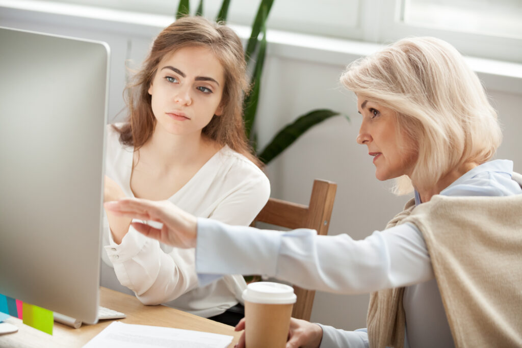 Photo of senior and young female colleagues discuss online project look at pc screen