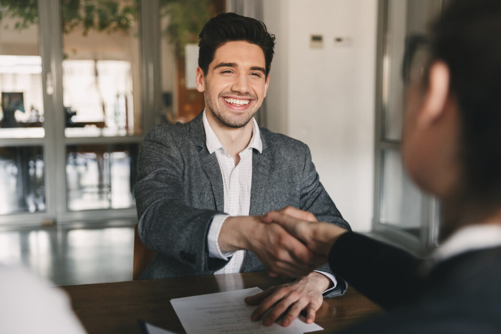 Photo of Business, career and placement concept - happy caucasian man 30s rejoicing and shaking hands with employee, when was recruited during interview in office.