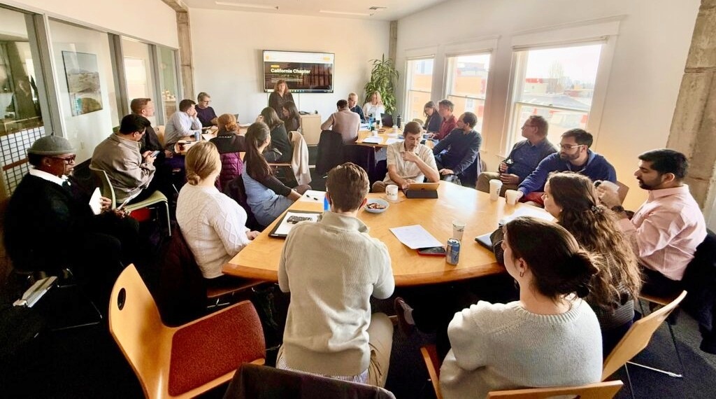 Photo of group of people sitting around a conference table listening to the speaker.