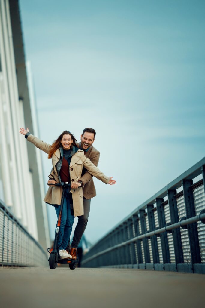 A joyful couple rides an electric scooter on a bridge, embracing the fun and excitement of urban transportation. Their carefree expressions capture a moment of happiness and adventure.