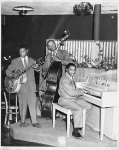 Photograph of musicians Bob Lewis (bass), Norvell Randell (piano), Eric Miller (guitar) on stage at Slim Jenkins Bar and Restaurant Oakland, California, circa 1950s.