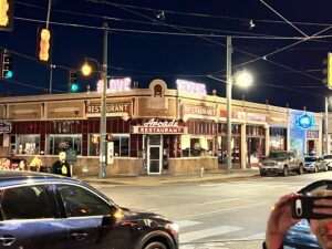 Photo taken at night of the front of a restaraunt on a busy street corner.