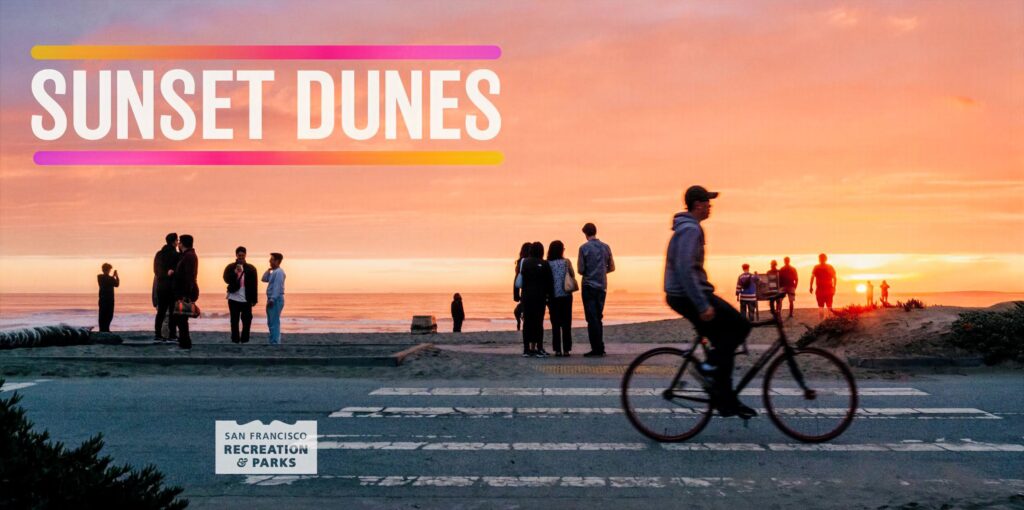 image showing people on a beach watching the sunset with a person on a bicycle riding by.