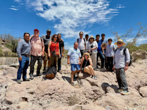 Photograph of a group of people posing on a rocky outcrop after touring Ranchero Viejo of Santa Cruz with Latino ranchers as guides on a beautiful day with mild temps and blue skies.