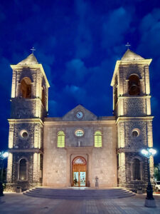 Nighttime photograph of the Cathedral of Our Lady of La Paz in La Paz, Baja California Sur, Mexico, lit up on the outside to accentuate the windows, roof lining, and front of the building.