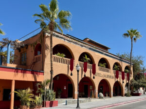 Picture of the outside of the Hotel California with palm trees flanking either side of the building in the town of Todos Santos, located on the Pacific Coast of Baja California Sur, Mexico.