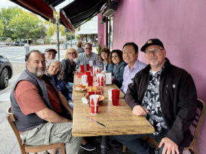 A picture of a group of people sitting around an outdoor cafe table smiling for the camera.