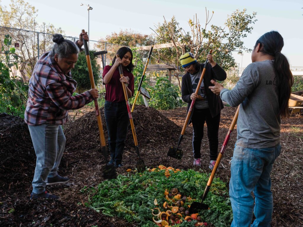 LA Compost Image of three volunteers and an LA Compost coordinator mixing in food scraps with woodchips, making compost