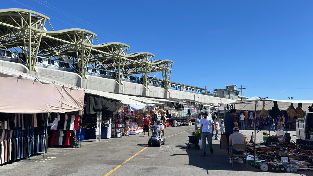 Bustling flea market under the Berryessa BART station platform, with a BART train sitting on the track.