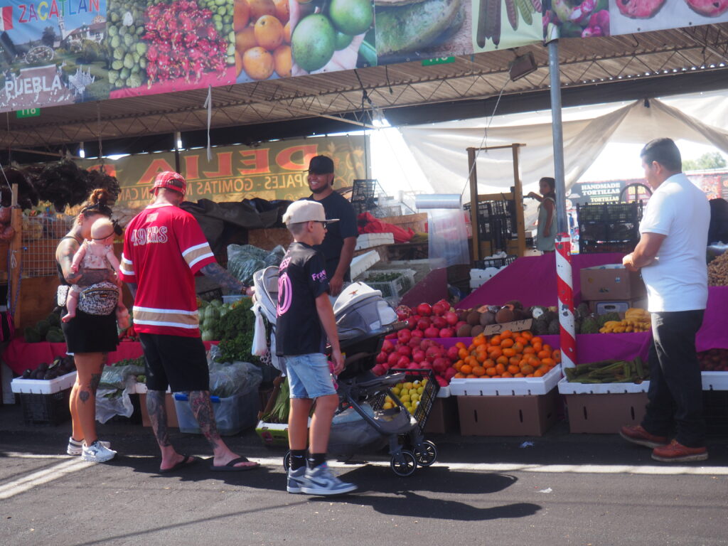 People&Produce Bustling produce section of the market with a family visiting a produce vendor’s stall.