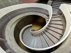The image shows a curving stairway made of white cement and marble, resembling the inside of a seashell or snail shell.