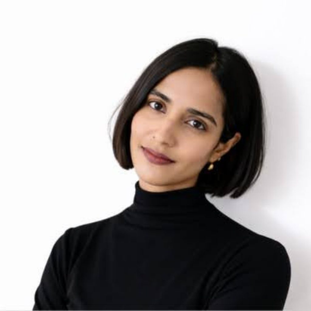 Headshot of a smiling young woman with short straight black hair and brown eyes, wearing a black turtleneck sweater.