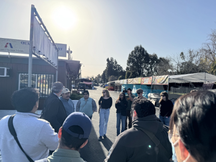 Roberto Gonzalez Mtg A class of students engaging in an outdoor discussion and site visit with a community leader at the Berryessa Flea Market.